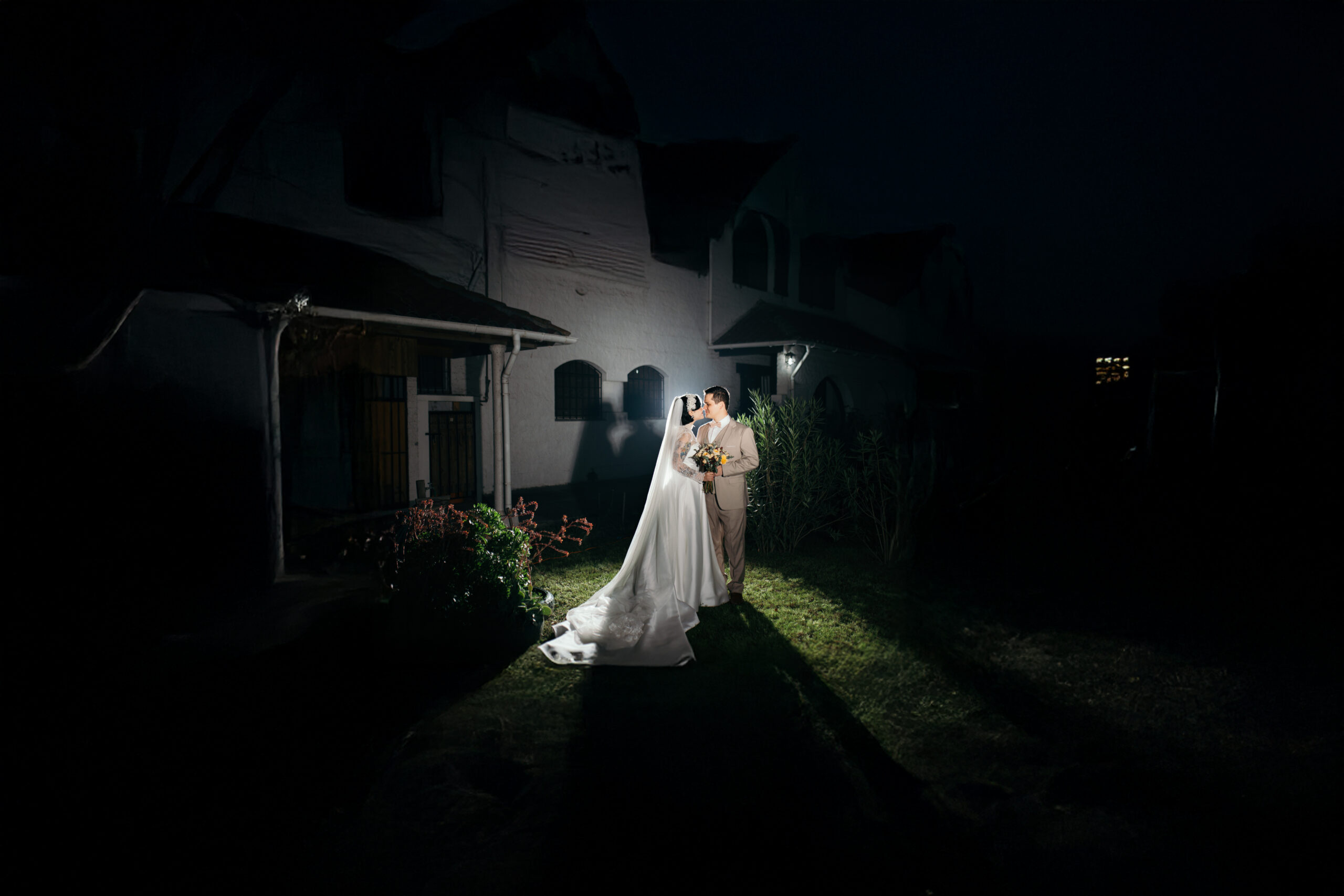 Fotografía nocturna de novios abrazados frente a una casa iluminada en su matrimonio, Bodafilms Santiago