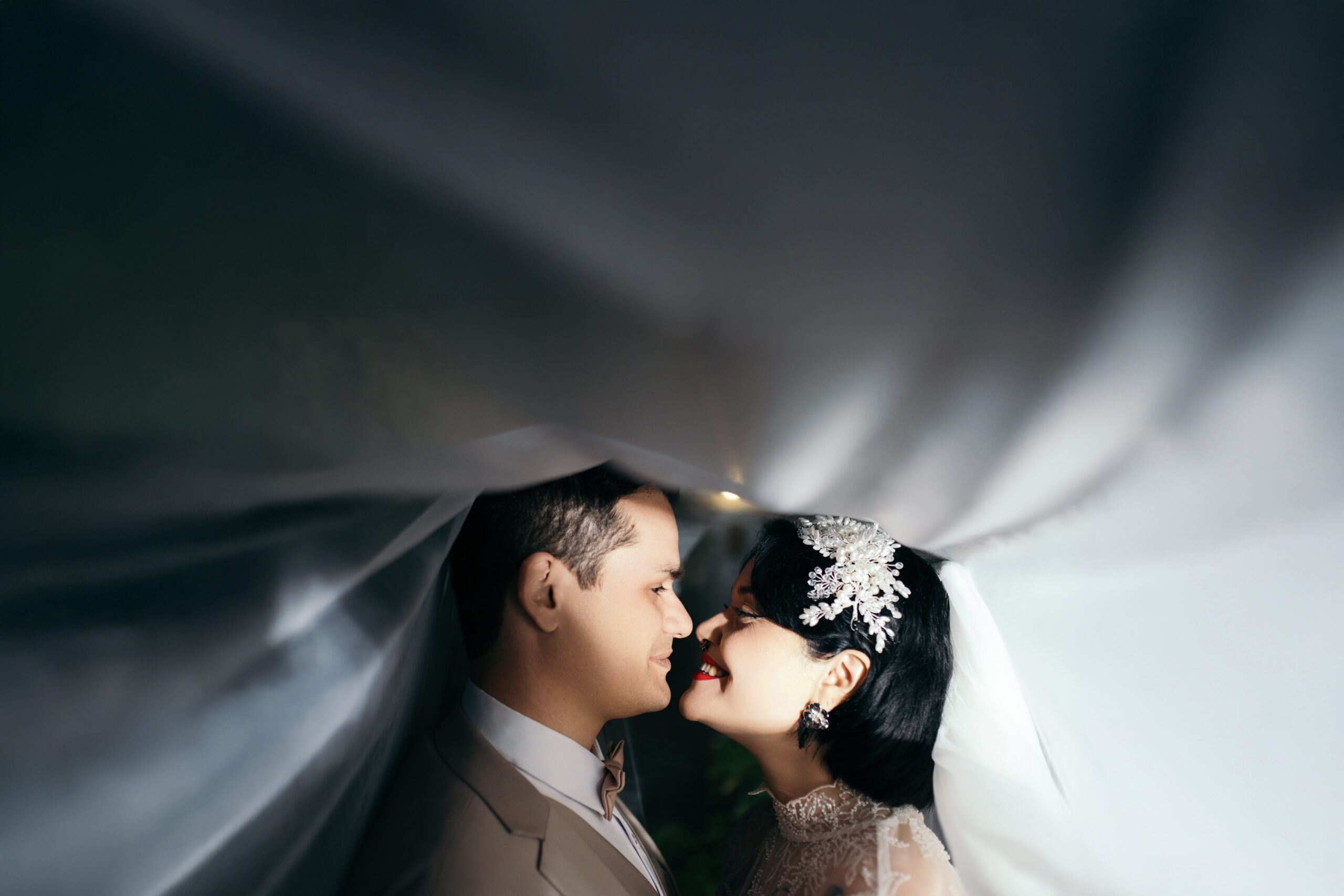 Novios a punto de besarse bajo un velo iluminado, retrato íntimo de matrimonio por Bodafilms en Santiago