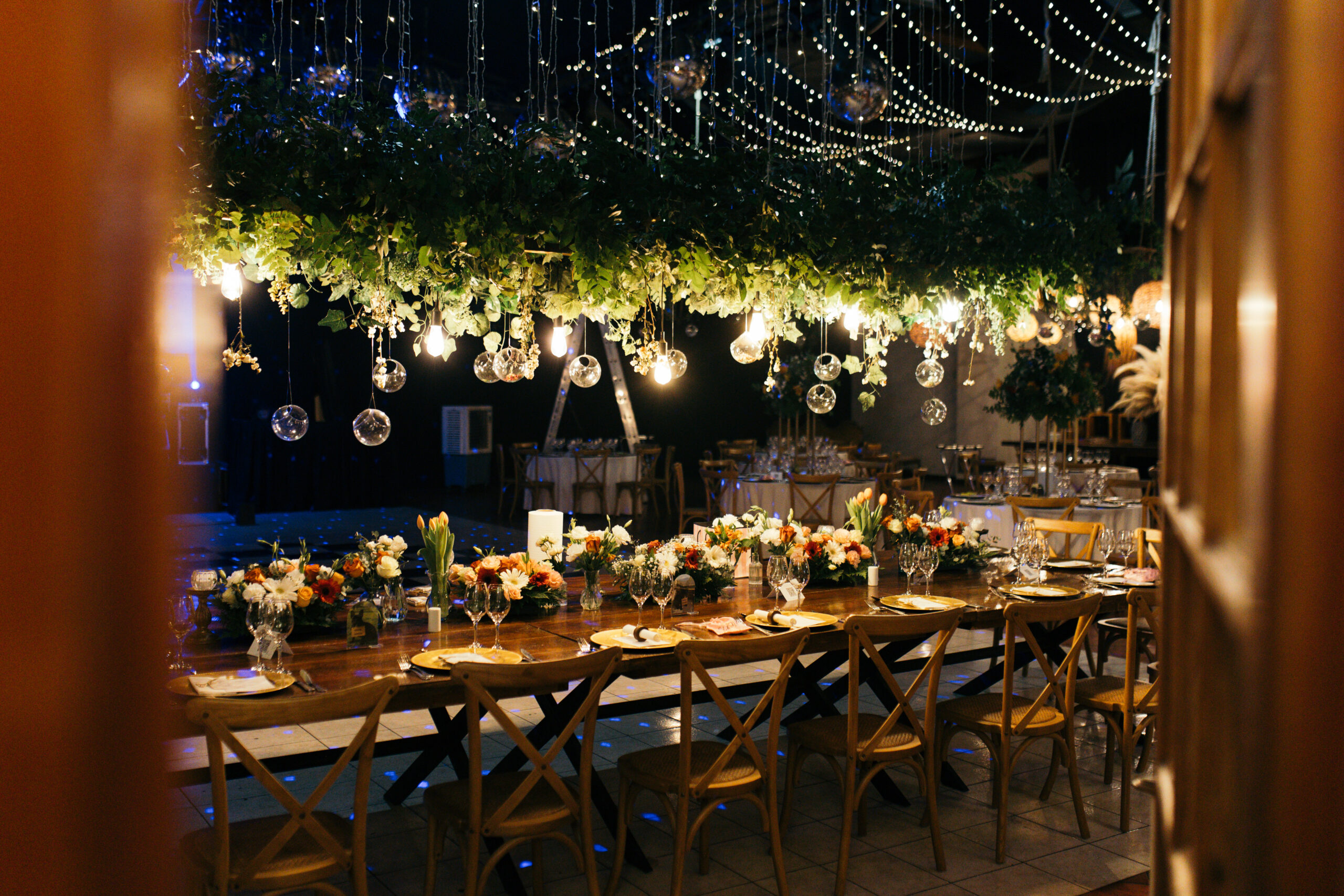 Montaje de mesa elegante para matrimonio, con luces cálidas colgantes en un entorno romántico.
